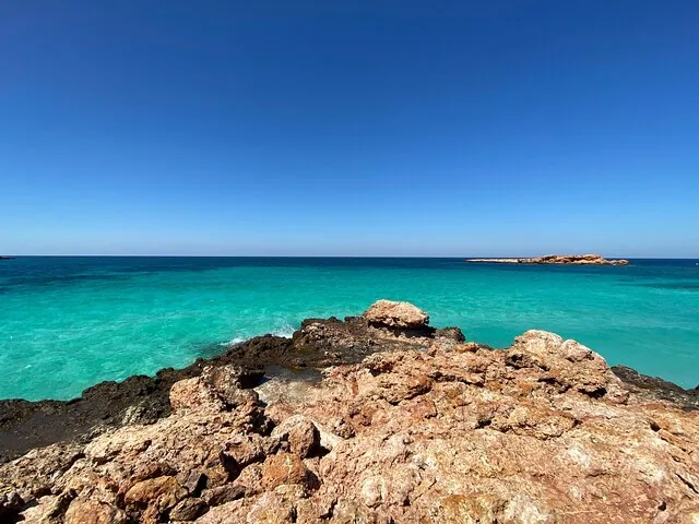 Felsige Küste, die in leuchtend türkisfarbenes Wasser unter klarem blauem Himmel übergeht.