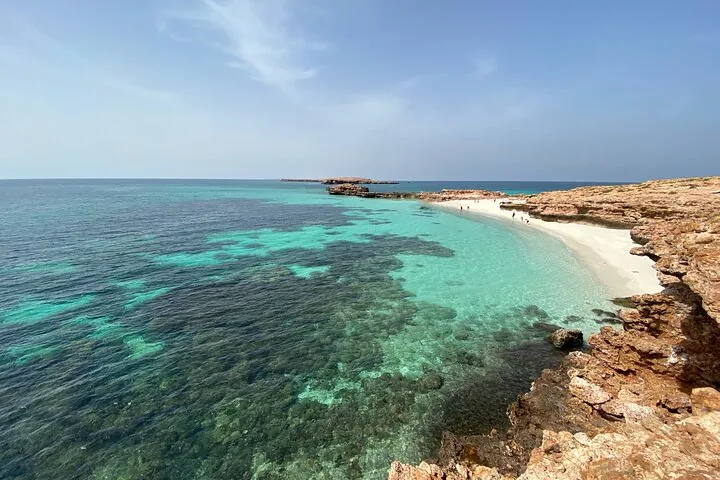 Malerischer Blick auf einen Sandstrand und flaches türkisfarbenes Wasser bei felsigen Inseln.