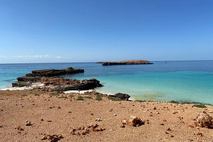 Una costa rocciosa che conduce ad acque basse, limpide e turchesi, con isole in lontananza.